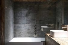 a chalet bathroom clad with grey stone tiles, done with beautiful wood, white appliances and a large mirror is cool