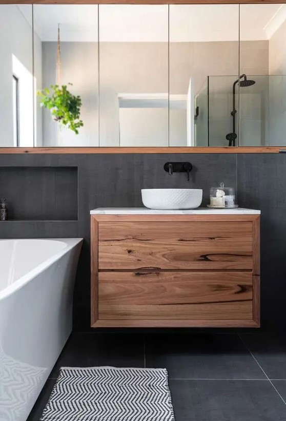 a contemporary bathroom clad with concrete tiles, a floating vanity, a mirror storage unit, a bathtub and niches for storage