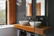 a contemporary bathroom clad with grey tiles of various shades, a bathtub, a floating vanity, wooden mats and accents