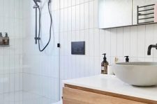 a contemporary bathroom clad with skinny tiles, with a floating timber vanity, a shower space, a mirror and black fixtures for a contrast