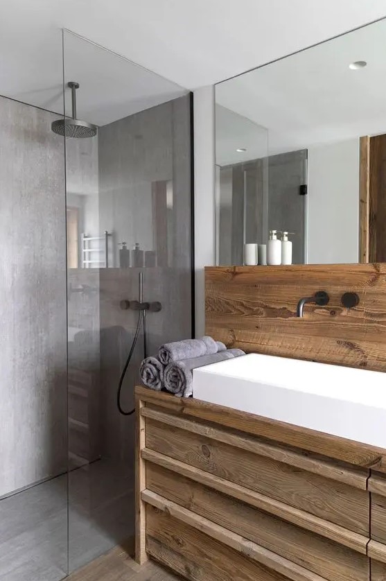 a contemporary bathroom clad with wood and with lots of concrete in decor, with a large mirror, a white sink and a rainshower