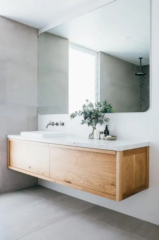 a contemporary bathroom with a wood and stone floating vanity, a large mirror and large scale grey tiles