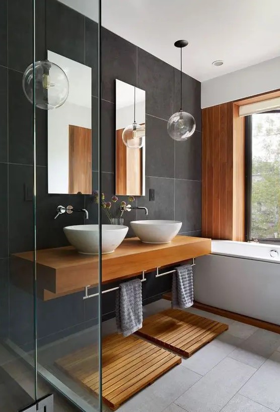 a contemporary bathroom with large scale dark grey tiles, a wooden accent wall, a floating timber vanity and mats