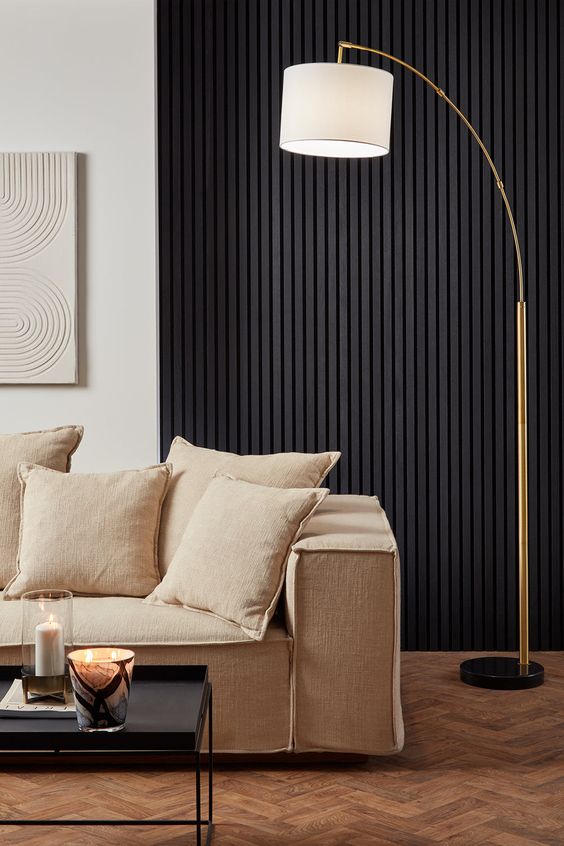 a contemporary living room with a black wood slat wall, a neutral sofa with pillows, a black coffee table and a floor lamp