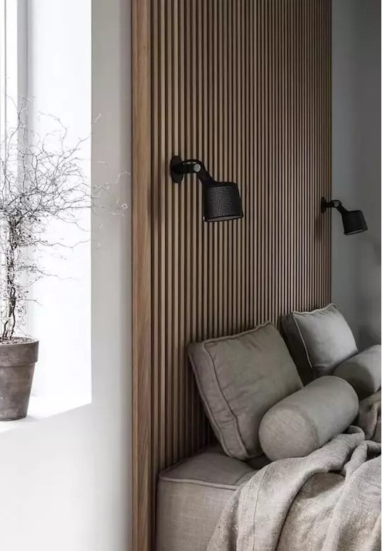 a contemporary neutral bedroom with a wood slat accent wall that features a couple of sconces, a grey upholstered bed and grey bedding, a potted plant
