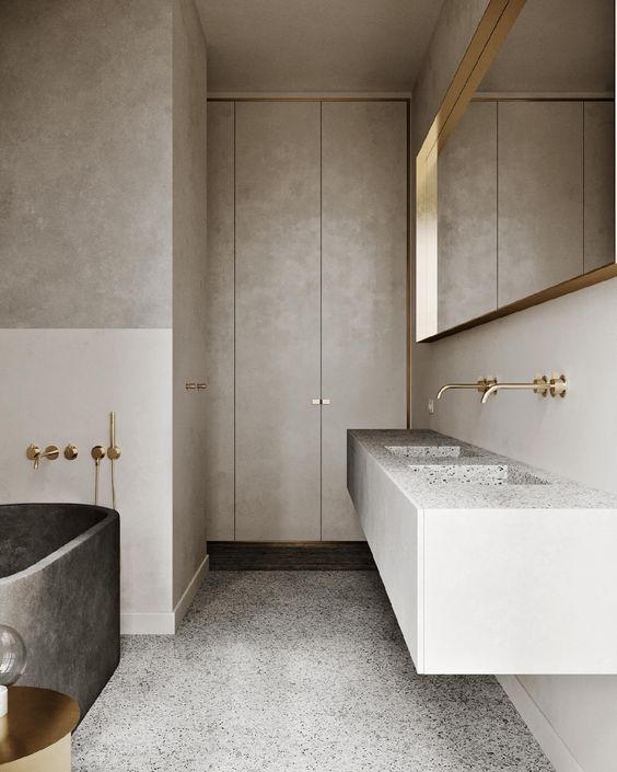 a contemporary to minimalist bathroom done in neutrals, with a large mirror in a gold frame, with a stone slab double sink and a dark stone bathtub, gold fixtures is chic