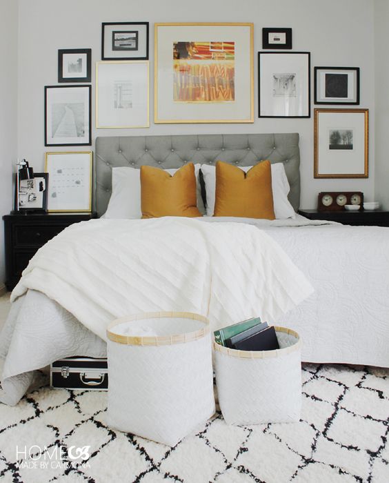 a contrasting bedroom with a grey upholstered bed and neutral bedding, baskets for storage, black nightstands and a lovely gallery wall