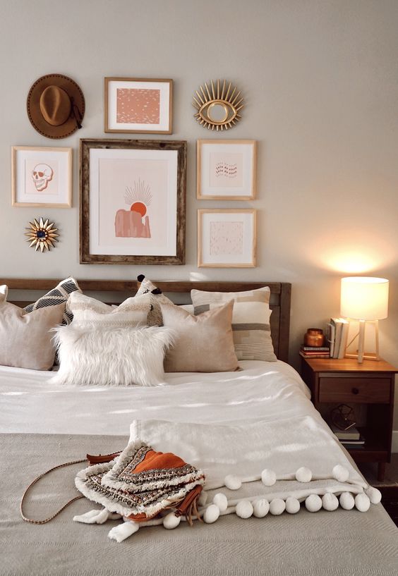 a cool boho bedroom with a stained bed and nightstands, a bright boho gallery wall, neutral bedding and a pompom blanket