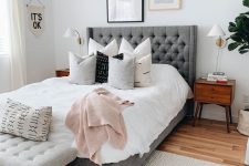 a farmhouse bedroom with a grey upholstered bed and neutral bedding, a grey upholstered bench, a small gallery wall over the bed and a cool chunky rug