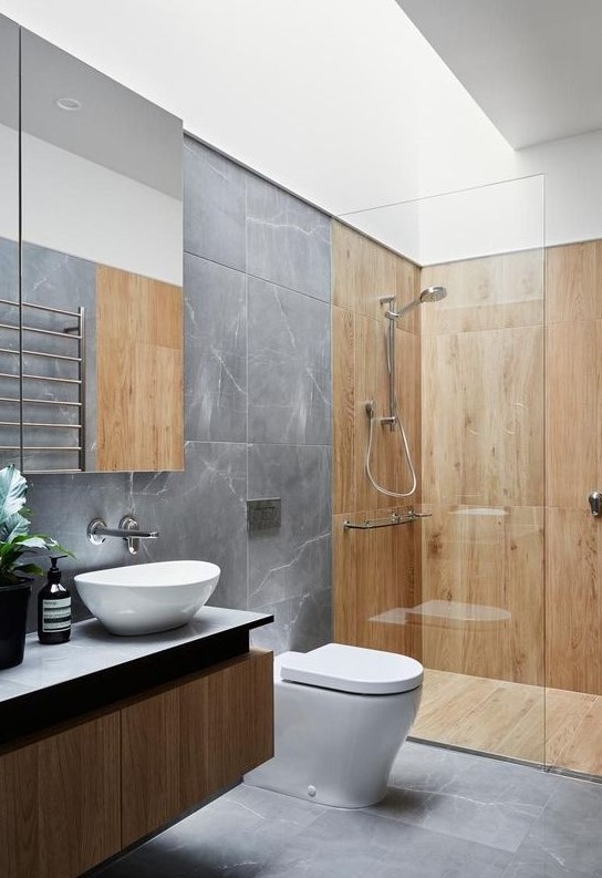 a grey marble bathroom with light-colored wooden tiles, a floating timber vanity, potted plants and a large statement mirror
