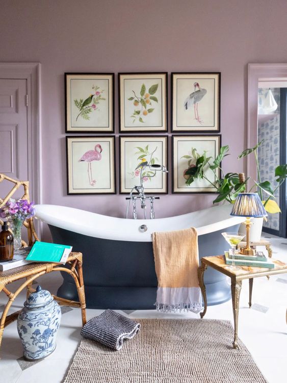 a lilac vintage bathroom with a chic gallery wall, a navy oval tub, a rug and some lovely coffee tables plus potted greenery