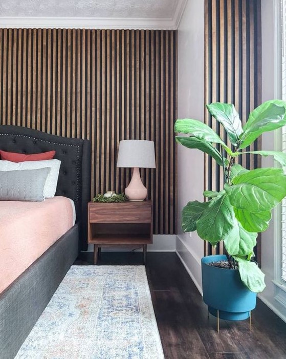 a mid-century modern bedroom with a wood slat accent wall, a graphite grey upholstered bed and a stained nightstand