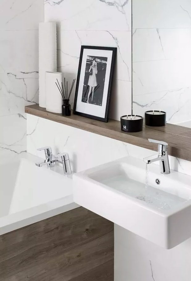 a minimalist bathroom clad with white stone tiles, a bathtub clad with wood, a wooden shelf and a small floating sink for a chic look