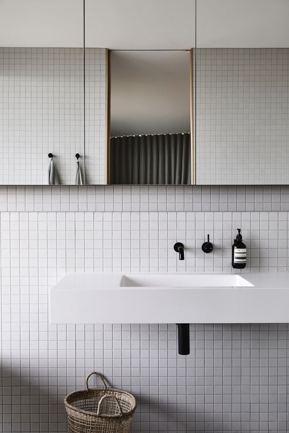 a modern bathroom clad with square tiles, a mirror with cabinets, a floating sink and black fixtures