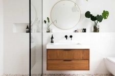 a modern bathroom in white, with a terrazzo floor, a wooden floating vanity and touches of gold