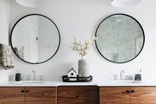 a modern bathroom with grey hex tiles on the floor, a rich-toned floating timber vanity and round mirrors