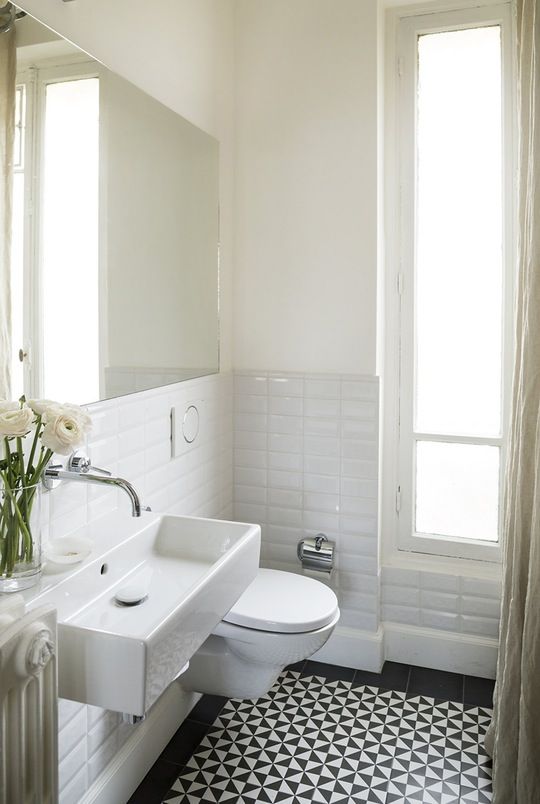 a modern black and white bathroom with a black geo tile floor, a floating sink, white tiles, a large mirror is a chic idea that looks cool