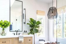 a modern country bathroom with white skinny tiles, a stained vanity, an oval tub, a pendant lamp and a skylight