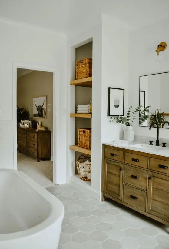 a modern country bathroom with white subway and hexagon tiles, a stained wooden vanity and built in shelves plus an oval tub