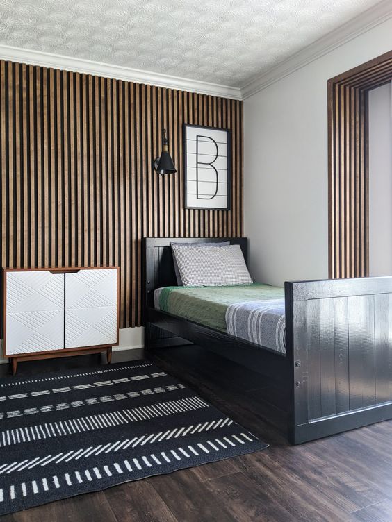 a modern kid's room with a wood slat accent wall, a black bed with bright bedding, a black and white rug and a dresser