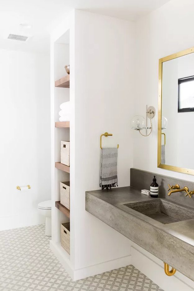 a modern neutral bathroom with built-in shelves, a built-in concrete sink, gold fixtures and a tiled floor is cool