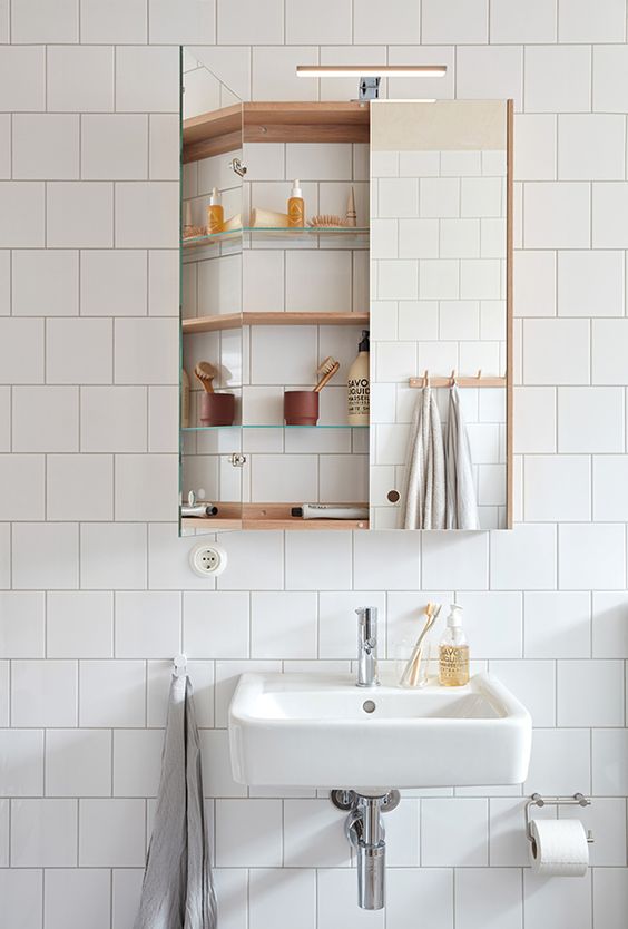 a modern white bathroom with a mirror storage cabinet, a floating sink and some light-stained wood is a lovely and airy space
