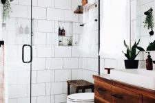 a modern white bathroom with various types of tiles, a dark stained floating vanity and a matching mat and bench, potted greenery