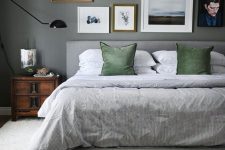a moody grey bedroom with a grey upholstered bed with grey and grene bedding, stained nightstands, a free form gallery wall