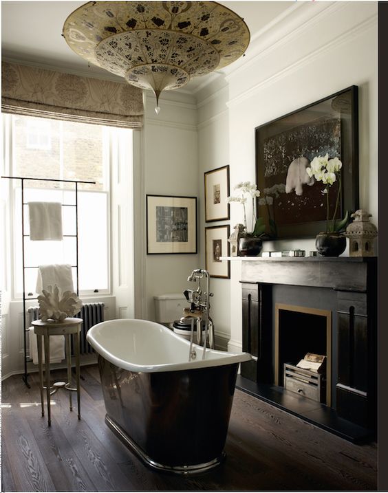 a moody vintage bathroom with a vintage fireplace, a black bathtub, a gallery wall and printed curtains and a printed pendant lamp