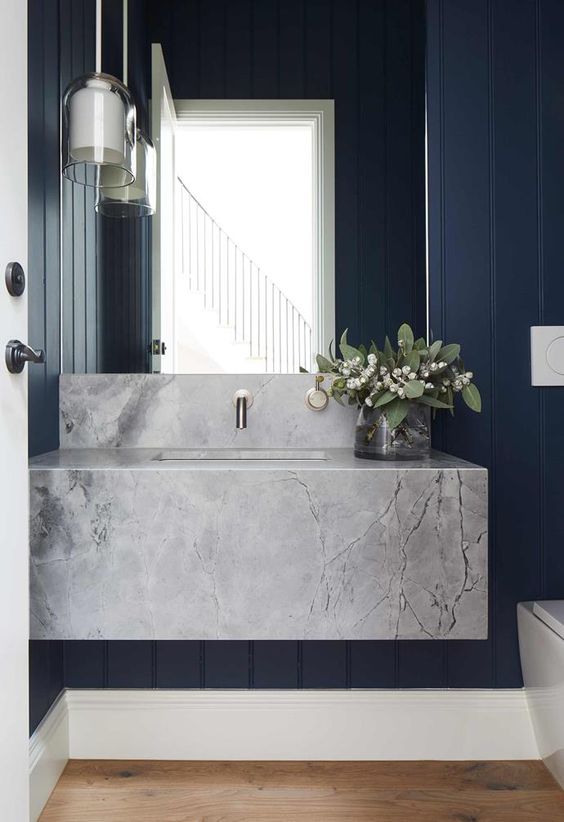 a navy powder room with a large grey stone slab floating sink, a pendant lamp and greenery and blooms
