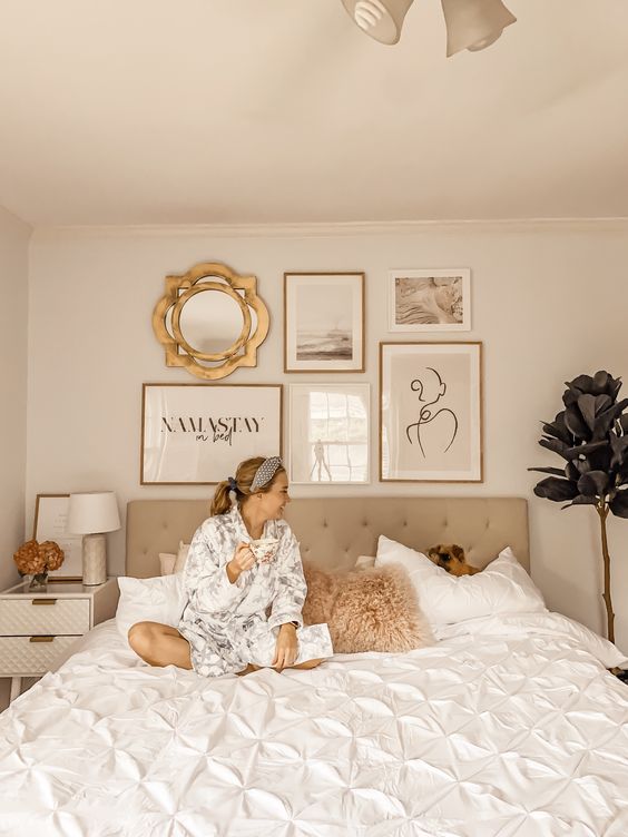 a neutral bedroom with a grey upholstered bed, neutral furniture, a chic gallery wall over the headboard and a creamy nightstand