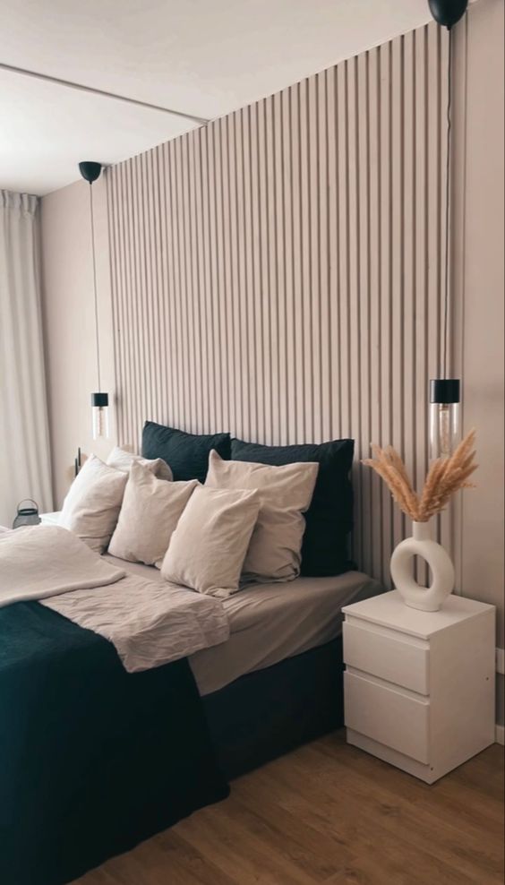 یک اتاق خواب خنثی با دیوارهای خنثی و یک ترمووال چوبی، یک تخت با ملافه های سبز و خاکستری، میزهای خواب سفید و دیوارکوب های خنک