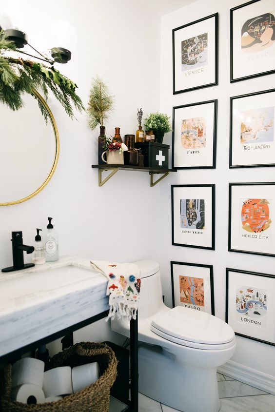a pretty and lovely bathroom with a colorful gallery wall, a sink on a metal and stone vanity, greenery and apothecary bottles