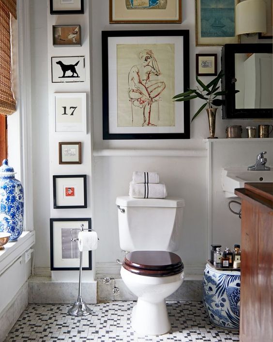 a pretty bathroom with blue and white tiles, a dark-stained vanity, a woven curtain and a gallery wall that takes all the blank space here