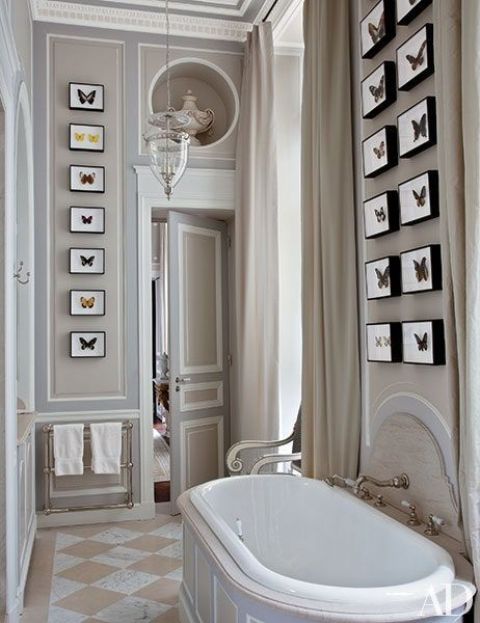 a refined tan and white bathroom with a checked floor, grid gallery walls with faux butterflies and some sophisticated vases and decor
