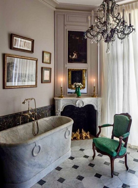 a refined vintage bathroom with a stone bathtub, a non-working fireplace, a green chair, a refined crystal chandelier and a gallery wall