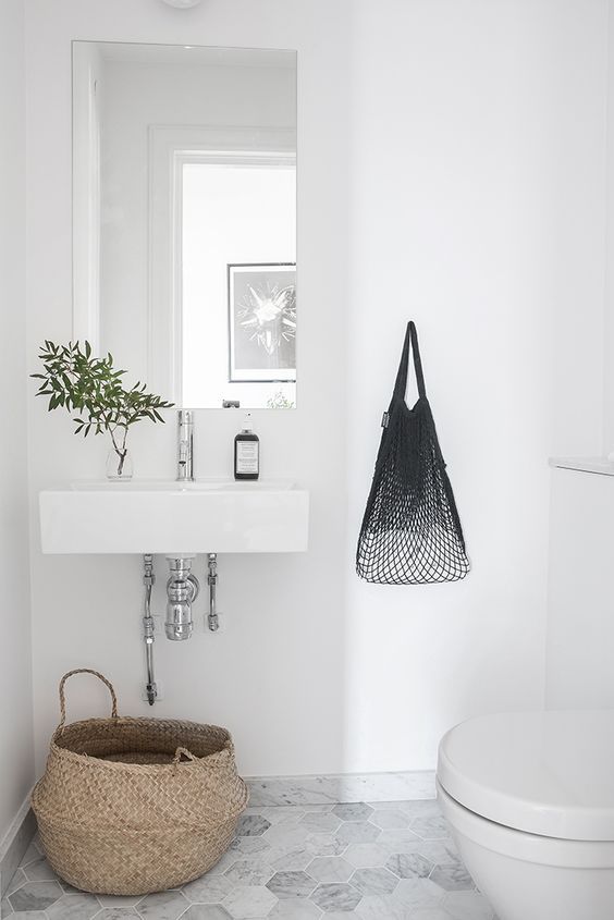 a small Nordic powder room with a white floating sink, marble hex tiles on the floor, a toilet and a basket for litter is cic
