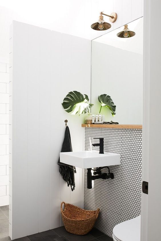 a small and cool contemporary bathroom done with white panels and penny tiles, a floating sink, black fixtures, a brass sconce and a large mirror