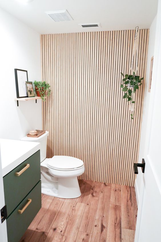 a small and lovely powder room with a wood slat accent wall, a green floating vanity, a shelf, some decor and greenery