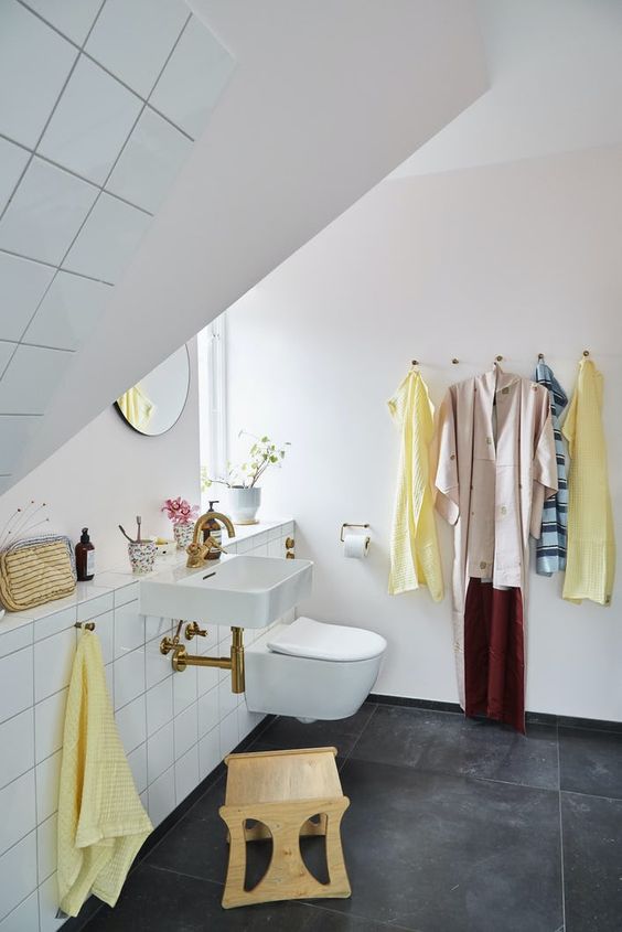 a small attic bathroom with black large scale tiles and white square ones, a floating sink, a round mirror and a plywood stool is cool