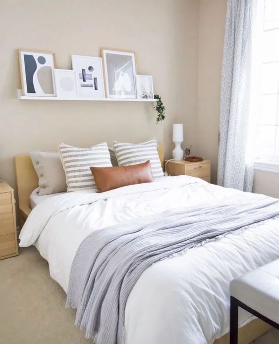 a soothing bedroom with tan walls, a stained bed and nightstands, neutral and blue textiles, a ledge gallery wall over the bed