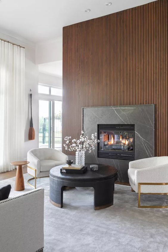 a sophisticated living room with neutral walls, a rich-stained wood slat wall with a built-in fireplace, white chairs and a round coffee table