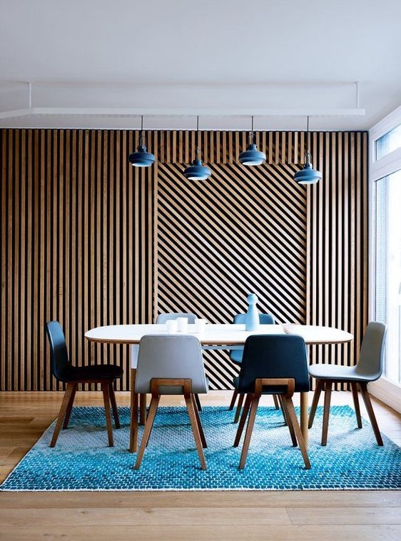 a stylish dining room with a wood slat accent wall, an oval table and navy and white chairs, pendant lamps over the table