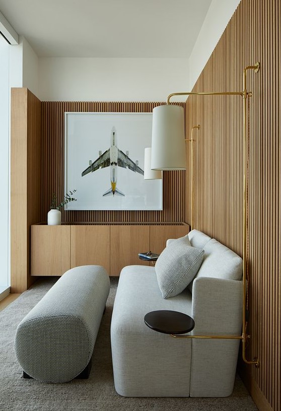 a stylish living room with wood slat walls, a grey loveseat and a footrest, a built-in credenza and some wall lamps