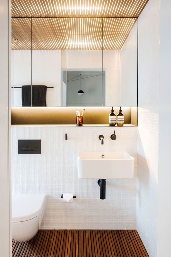a stylish modern powder room with a large lit up mirror cabinet, a floating sink, a wooden plank floor and white tiles