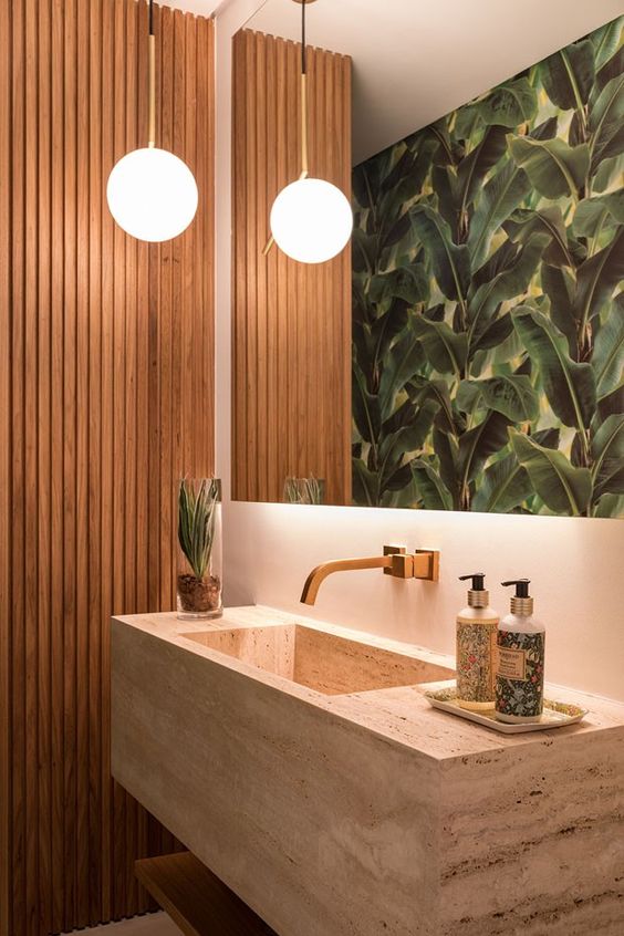 a tropical bathroom with a wood slab accent wall, a large mirror, a tropicla leaf wall, a stone floating sink and a bold pendant lamp