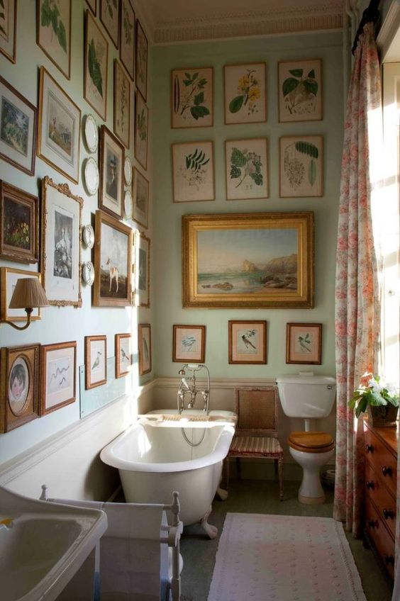 a vintage bathroom with light green walls, a gallery wall that covers two walls at once, a clawfoot bathtub and a free-standing sink