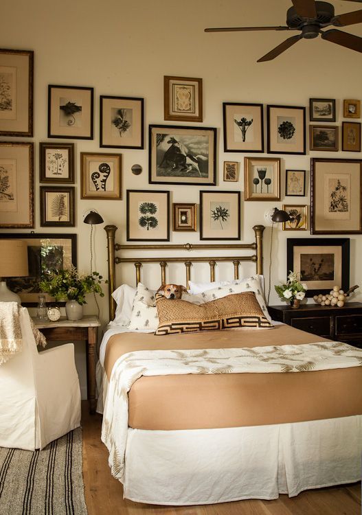 a vintage bedroom with a brass bed with printed bedding, stained nightstands and dressers, a large vintage gallery wall