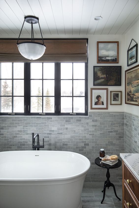 a vintage cottage bathroom with grey tiles, a vintage gallery wall, a modern soak tub and a black side table