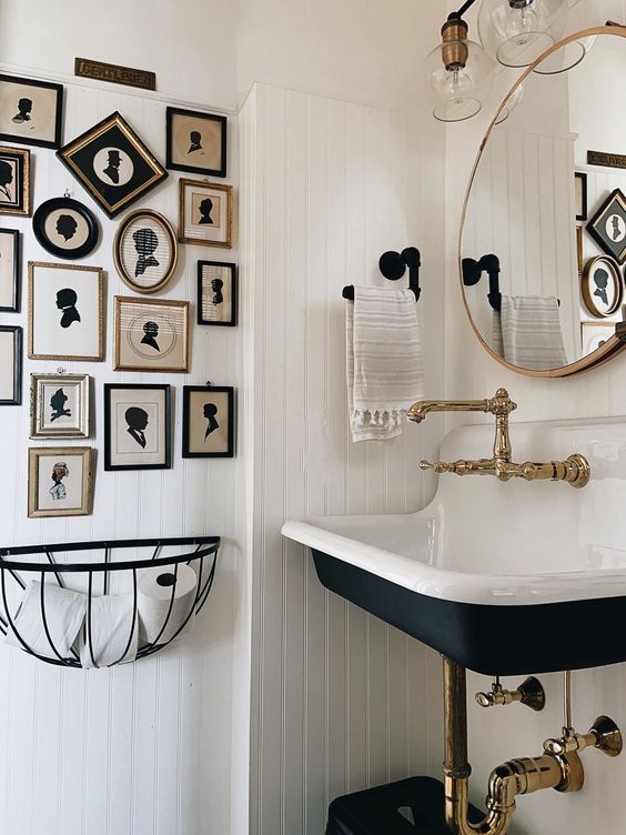 a white farmhouse bathroom with planked walls, a navy wall-mounted sink, a vintage silhouette gallery wall and vintage fixtures